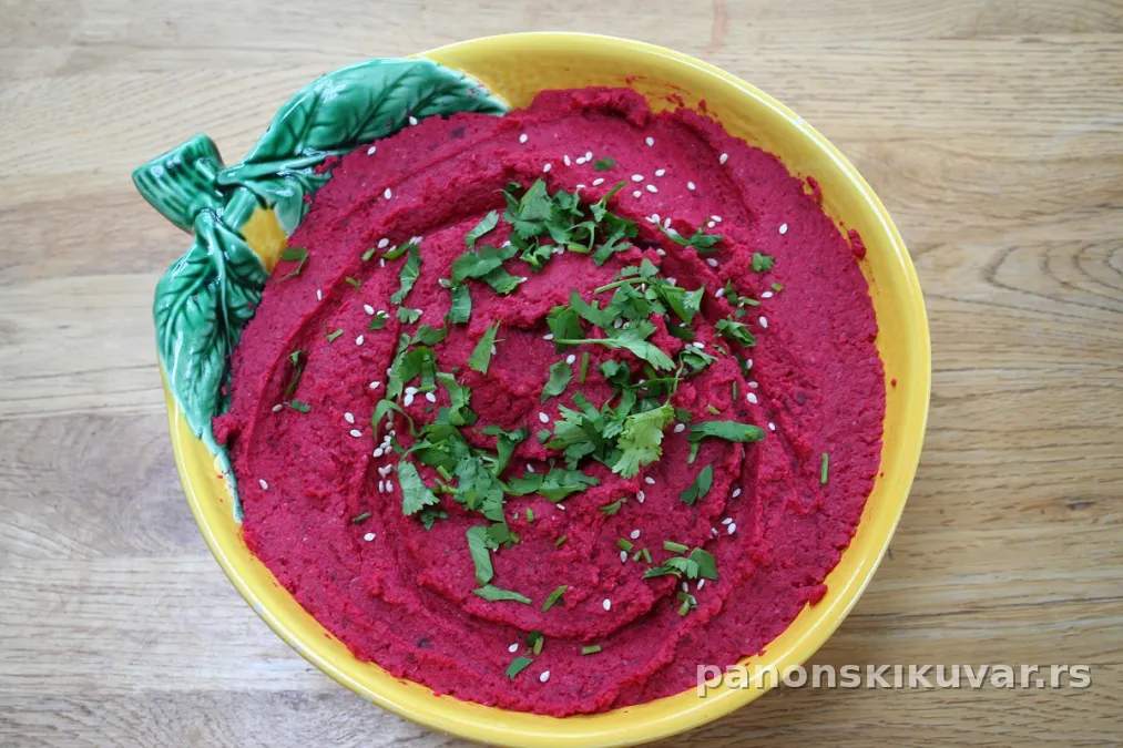 Kremasti roze humus od cvekle u činiji ukrašen maslinovim uljem i peršunom
