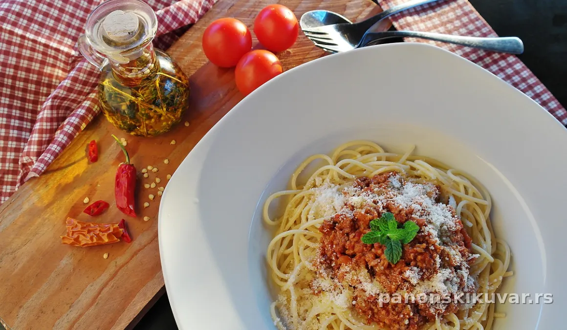 Tanjir špageta prelit bogatim bolonjeze sosom i posut parmezanom na drvenom stolu