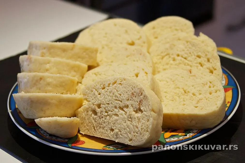 krupni kolutovi knedle od hleba posuti rendanim sirom, servirani na belom tanjiru