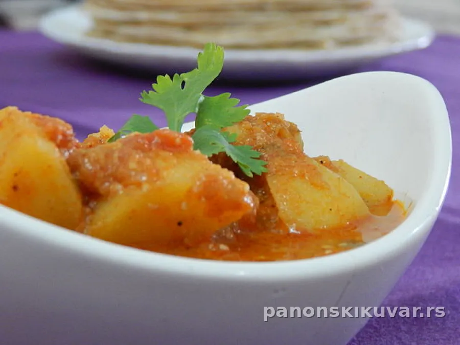 Topao krompir paprikaš u dubokom tanjiru, crvena paprika i peršun na vrhu