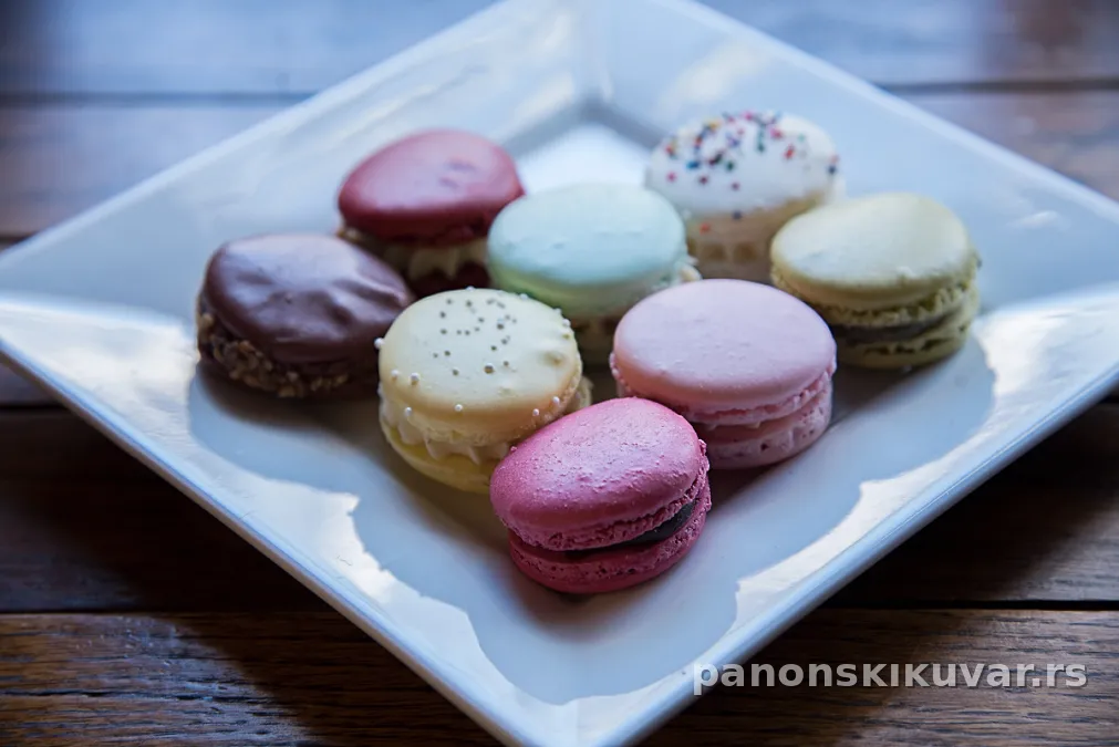 Šareni macarons sa glatkim kremom, poređani na drvenoj dasci u različitim bojama i ukusima