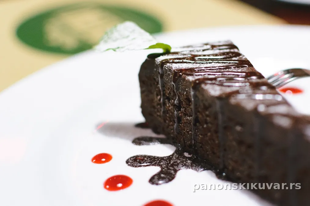 okrugla čokoladna torta prelivena sjajnim čokoladnim prelivom, sečena i posuta čokoladom