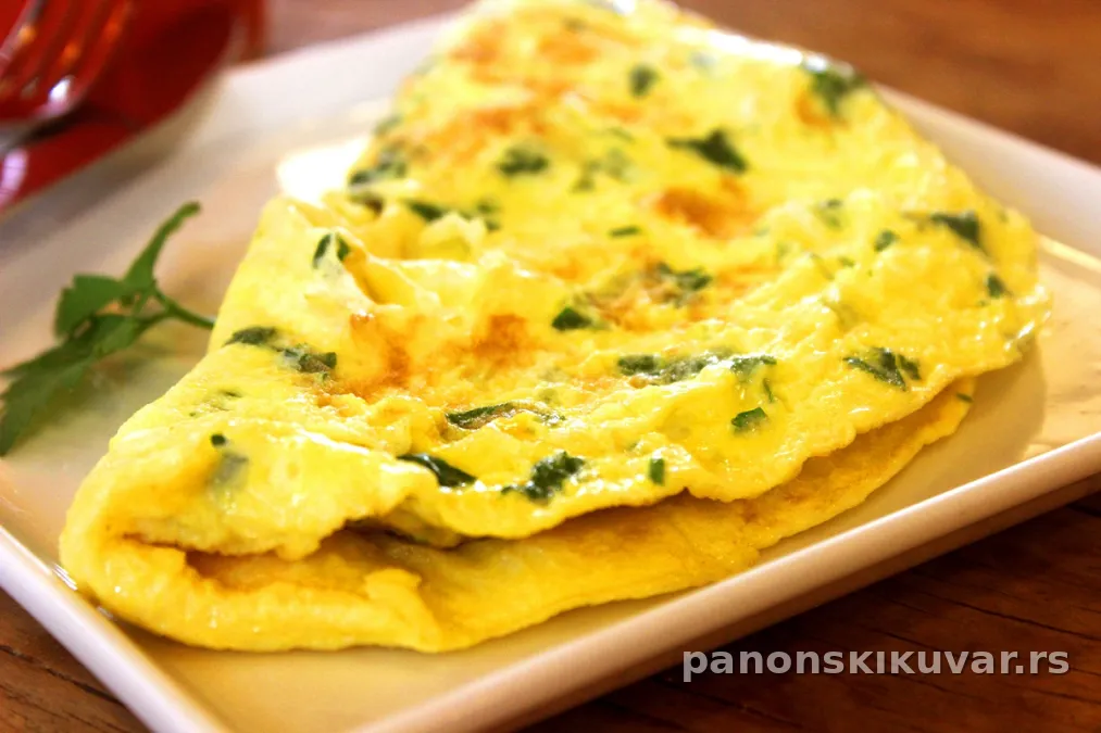 zlatno braon omlet sa komadićima špargli i posutim parmezanom na belom tanjiru