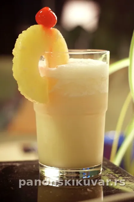 visoka čaša pina colada sa kriškom ananasa i crvenom trešnjom na vrhu