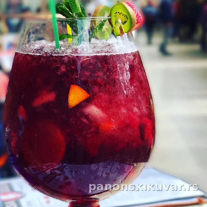 čaša sangrije sa šarenim kockicama voća i kriškama breskve i listićima nane