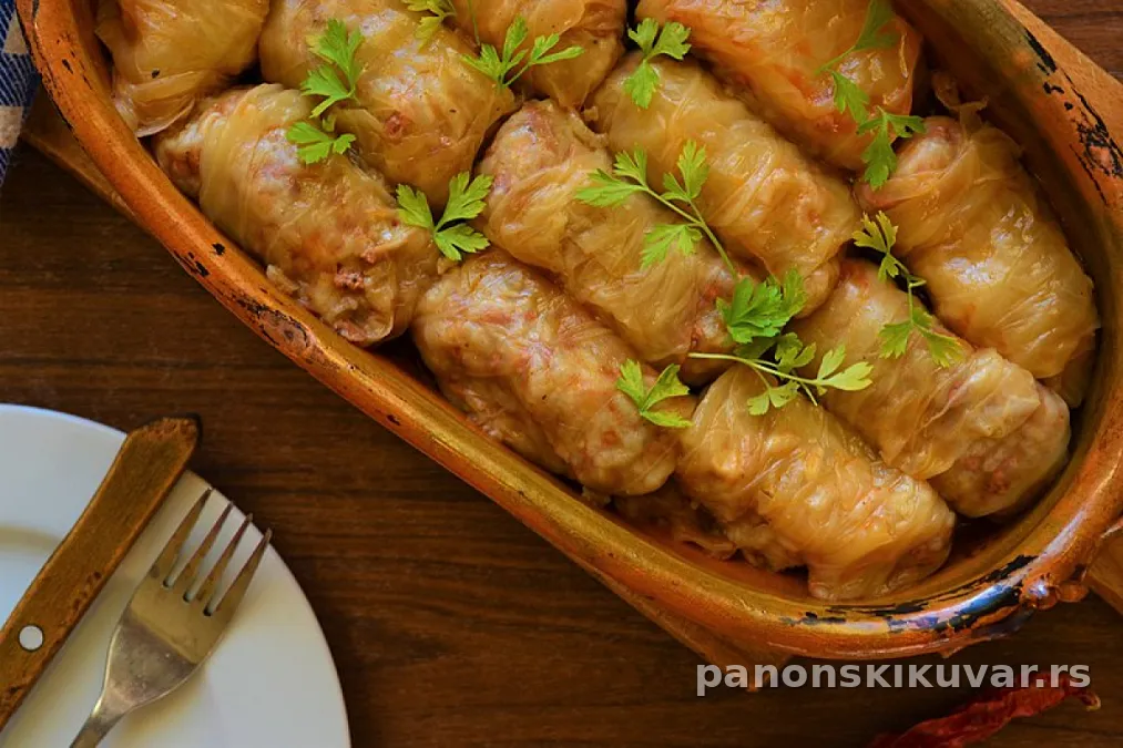 tople sarma rolnice složene u šerpi sa dimljenom šunkom i peršunom