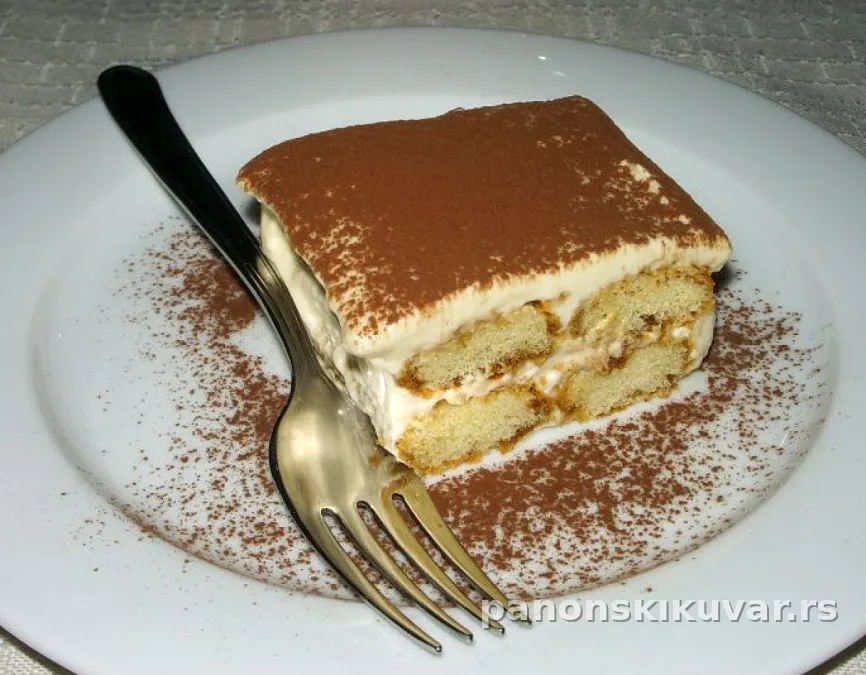 parče tiramisua sa kremom od sira, posuto kakaom i piškotama u pozadini